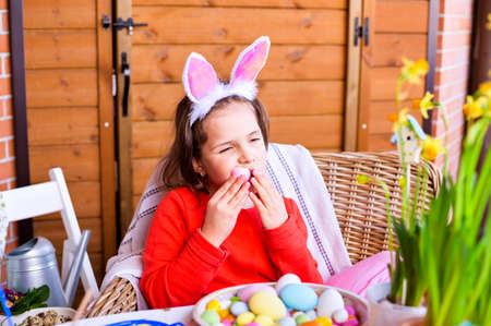 happy Easter. Little girl with colored eggs in her hands and chocolate colored eggs. Happy Easter holiday at home. Decor and decoration on the table. Copy space.の写真素材