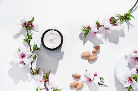Jar with cream on a light background. Hand care lotion with almond oil and vitamins. Body skin health and beauty. A bright background, cosmetics and natural almond flowers. Mockup. Copy spaceの写真素材