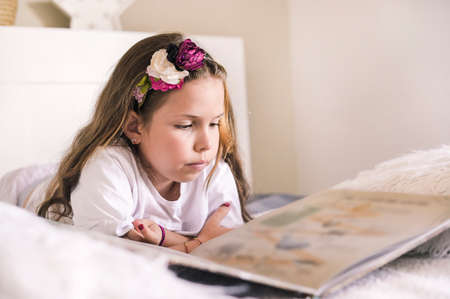 Schoolgirl reading a book in the room. Girl 8 or 10 years old with a book in the room on the bed. A...