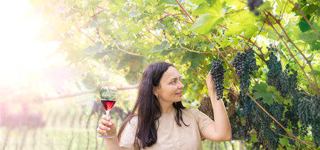 Beautiful woman dreaming tasting red wine enjoying summer stay in vineyards on lovely sunny day. woman drinking red wine at vineyard. harvest season. High quality photoの写真素材
