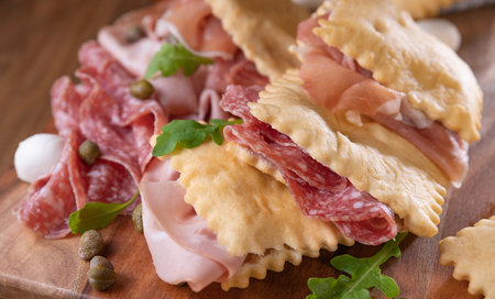 Crescentina. Food of Emilia Romagna region, deep fried bread gnocco fritto or crescentina. Starter or aperitif in Italy. Creshantina with prosciutto crudo, mortadella, Milanese salami, capers, cheeseの写真素材