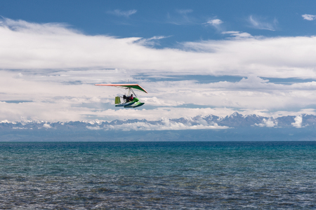 hang-glider hovering over pure emerald water of the lake near mountains