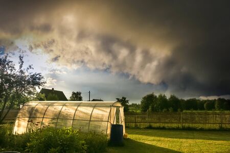 rural landscape with vegetable garden and greenhouse and garden against a stormy sky and clouds at sunsetの写真素材