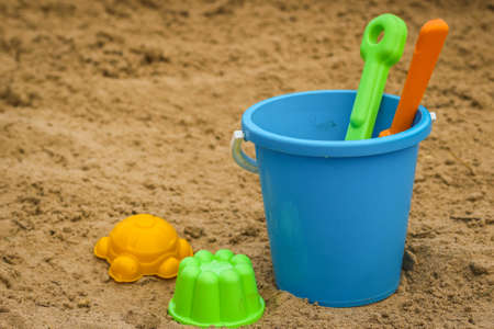 Children's beach sand toys. Kids concept. Plastic children's toys. Blue bucket, colorful molds. Kids toys, on sand beach in summer day.の写真素材