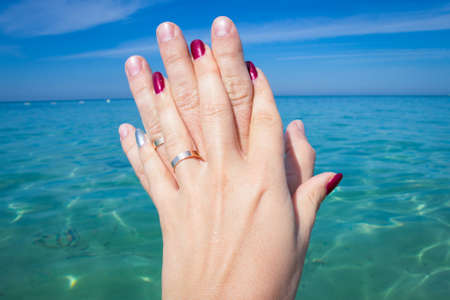 Holding Hands with wedding Rings on the sea Background. A romantic vacation, a love honeymoon. Vacation holidays relaxing concept.の写真素材