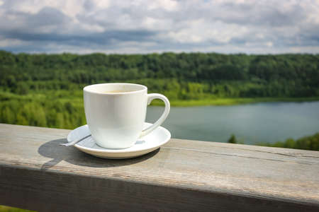 White cup of hot coffee on balcony with natural and mountains, hills background. Copy space. Beverage, breakfast.の写真素材