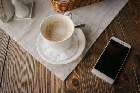 Top view of a smartphone and a Cup of coffee on a rustic wooden table. Morning concept. Beverage, breakfast.の写真素材