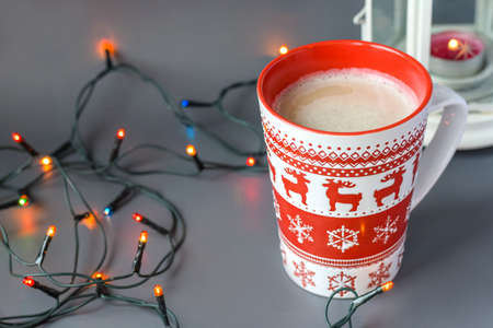 Red Christmas coffee mug. Cappuccino Cup with candles on a gray background. Selective focus.の写真素材