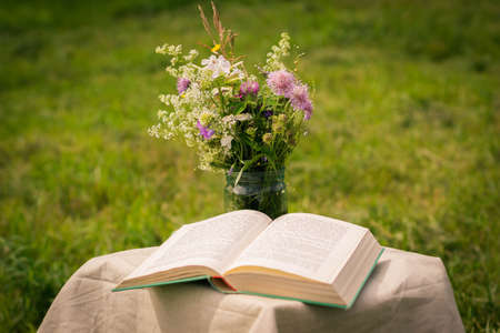 A beautiful bouquet of wildflowers and the open book on a soft green summer background of summer garden.の写真素材
