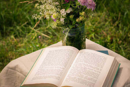 A beautiful bouquet of wildflowers and the open book on a soft green summer background of summer garden.の写真素材