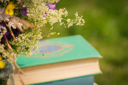 A beautiful bouquet of wildflowers and the books on a soft green summer background of summer garden.の写真素材