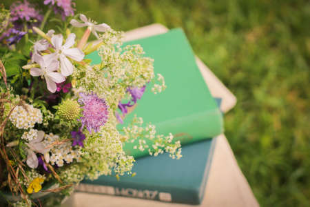 A beautiful bouquet of wildflowers and the books on a soft green summer background of summer garden.の写真素材