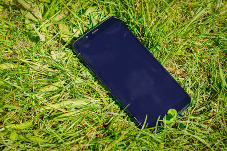 Mobile smart phone in green grass and black screen. Touch screen smart phone on the field of grass.