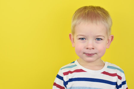 Happy smiling little boy on color background. Portrait of a beautiful European boy two years old on a yellow background. Copy space for text.の写真素材