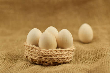 Decorative wooden Easter eggs in a wicker basket. Chicken eggs closeup on a vintage background. Zero...