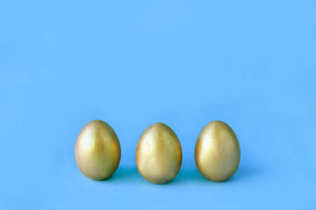 Easter eggs on blue background. Three golden eggs. Minimal style. Easter decorations. Happy Easter.の写真素材