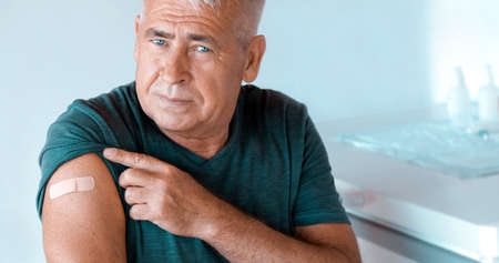 Male Senior smiling after Receiving  Vaccine. Elderly Man feeling Good on getting Vaccine .  Vaccination for Older People. Senior Man showing her Arm with Bandage, Patchの写真素材