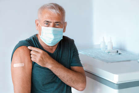 Male Senior in Face Mask after Receiving  Vaccine. Elderly Man feeling Good on getting  Vaccine.  Vaccination for Older People. Senior Patient showing Arm with Bandage, Patchの写真素材