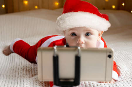 Smiling Baby Wearing Red Santa Claus Costume Making Video Call to Grandparents. Christmas Online...