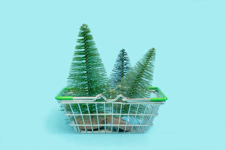 Small Christmas trees is in a shopping cart. Artificial mini Christmas tree in a supermarket trolley on blue background. Christmas, New Year, Holiday shopping concept. Minimalismの写真素材