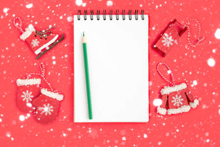Christmas presents preparation. Notebook, pencil, decorative snowflakes, mitten, sledge, skates on red background. Xmas and Happy New Year composition. Flat lay style, top view, overheadの写真素材
