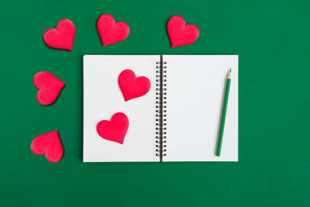Notebook with pencil, red hearts. Open notebook on green emerald color background, spiral notepad....
