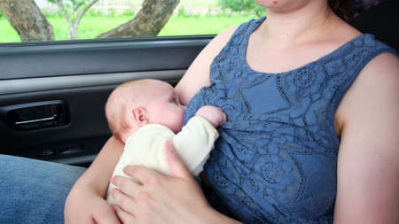 Mother breastfeeding child in a car, public breastfeeding. Mom holding adorable newborn baby in...