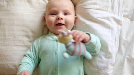 Cute Newborn Baby Lying on the Back and Plays with Colorful Toys. Little Three Month Child Takes a...