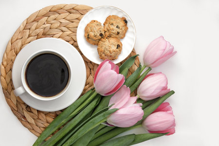 White cup of coffee with pink tulips on white background. Morning coffee on wicker tray. View from above of morning coffee, cookies and flowers. Flat lay. Breakfast in bed. Stylish home interior decorの写真素材
