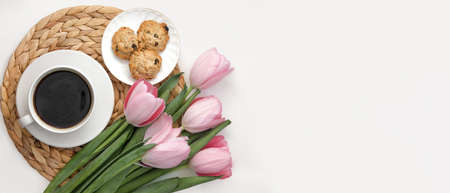 White cup of coffee with pink tulips on white background. Morning coffee on wicker tray. View from above of morning coffee, cookies and flowers. Flat lay. Breakfast in bed. Stylish home interior decorの写真素材