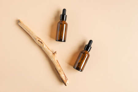 Dark amber glass bottle on beige background. Wooden branch. Natural skin care SPA beauty product design. Mineral organic oil cosmetics. Minimal Mock-Up. Oily pipette. Face and body treatment. Flat layの写真素材