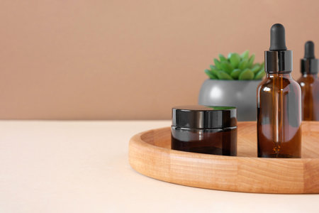Glass bottles on wooden plate. Natural skin care SPA beauty product design. Mineral organic oil cosmetics on beige background. Earth tones. Mock-Up. Oily pipette. Face and body treatment. Front Viewの写真素材