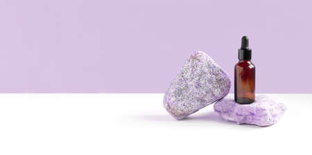 Dark amber glass bottle standing on stone. Natural skin care SPA beauty product design. Mineral organic oil cosmetics on violet background. mockup. Oily pipette. face and body treatment. front view.の写真素材