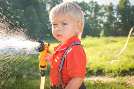 Cute little boy watering flowers in the garden. Young Child splashing Water from Garden Water Hose....