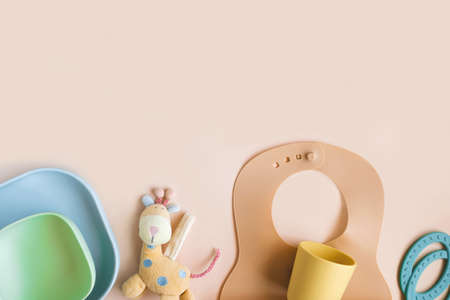 Baby accessories and tableware for food on beige background. First food for kids concept. Flat lay, Top View, Copy Space. Silicone plate, bib with on neutral background. Baby servingの写真素材