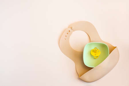 Baby accessories and tableware for food on beige background. First feeding for kids concept. Flat lay, Top View, Space for text. Silicone dishware, bib, cup on neutral backdrop. Serving baby food.の写真素材