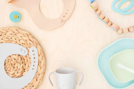 Baby accessories and tableware for food on wooden background. First feeding for kids concept. Flat lay, Top View, Space for text. Silicone dishware, bib, cup on neutral backdrop. Serving baby foodの写真素材