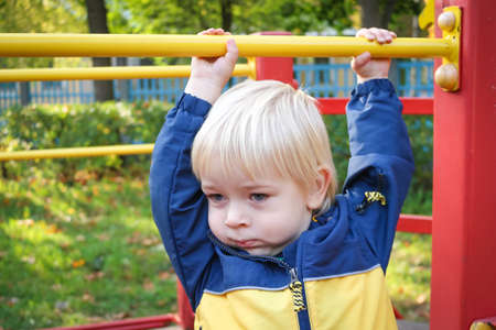 Portrait of two years old child boy at colorful playground area. autumn public park. Little blond...