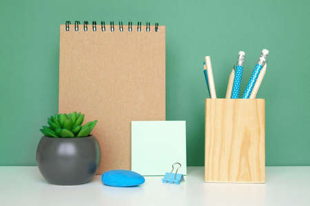 School equipment on white table, green wall background. education backdrop. Wooden school supplies, notepad, pencils and cactus plant. back to school. student desk. stationery for study. work at homeの写真素材