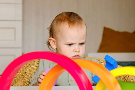 Little baby child in clothes made of natural fabric plays with rainbow colored wooden toys at white table. Cozy room background in scandinavian style. Warm natural colors. Eco friendly lifestyleの写真素材