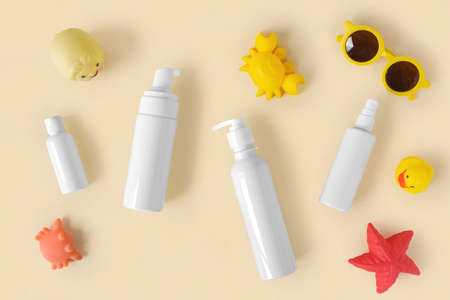 Sunscreen lotion tube on neutral background. Plastic bottle of sun protection and kids sunglasses and sandbox toys on beige table. Children's skin care concept. Sunscreen for kids. baby cosmetic.の写真素材