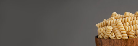 Gluten Free Cornmeal Pasta in wooden Bowl. Spiral Raw Macaroni from Blend of Corn and Rice flour. Close Up, Front View. Uncooked Bucati Pasta. food background. Horizontal banner with space for textの写真素材