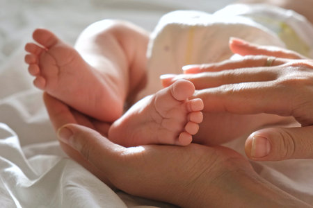 Baby feet in mother hands, on her palm. Happy parents holding their baby feet, close up. Maternity,...