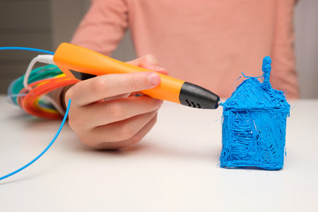 Teen Girl Using 3d Pen. Printing with Colored Plastic Wire Filament. Child making a House, drawing with 3D pen. Artwork, Robotics. STEAM, STEM education. Modern Technologies. Play and study at homeの写真素材