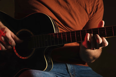 Man Playing Guitar with Neon Light. Unrecognizable Person Rehearing. Strumming Acoustic Guitar. Musician Plays Music. Male Fingers and Fretboard Close Up. Man Hand Playing Guitar Neck in a Dark.の写真素材
