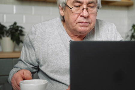 Senior male business owner in glasses sitting at desk in front of laptop. Successful older male...