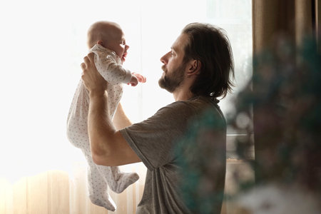 Young neo father is playing with his newborn baby in a nursery morning. father's day. Daddy holds in hands little Child and Plays with him. Concept of children, baby, parenthood, childhood, family.の写真素材