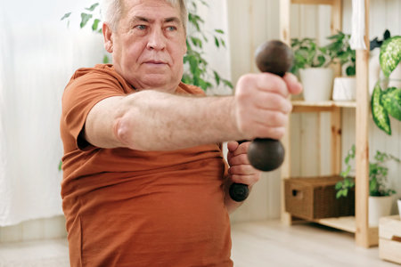 Old elderly man in sportswear training in living room doing weight lifting dumbbell exercising at home, Leisure healthy lifestyle.の写真素材