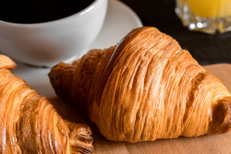 Coffee cup with croissant on a rustic dark wooden table. food series. Two tasty fresh croissants, jam, orange juice. Continental breakfast served with freshly baked pastry. close up view. good morningの写真素材