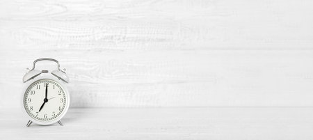 Front view white desk with alarm clock, coffee mug and copy space. Morning background banner with free space for text. Minimalistic concept, workspace, time to work. Blank workplace. Office mockup.の写真素材